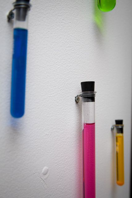 Glass test tubes filled with different color liquid and hung on a white wall
